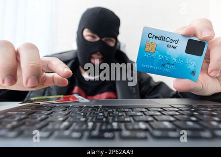 Uomo in maschera rapinatore utilizza internet, conto corrente bancario e di credito. Attacco di phishing da maschio con faccia nascosta. Il pirata informatico entra il furto di dati finanziari. C Foto Stock