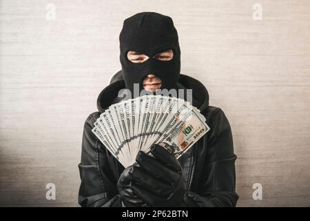 Primo piano ritratto di sneaky scassinatore con maschera nera e guanti che contano soldi su sfondo bianco. concentrarsi sul denaro. Foto Stock
