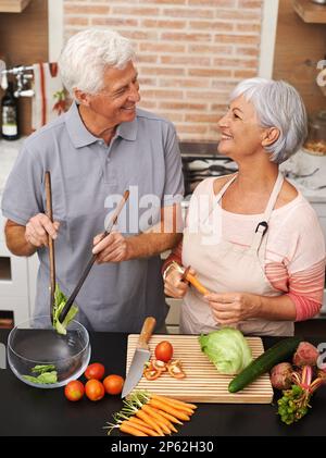 Una moglie sana è una vita felice. Romantico scatto di una coppia che condivide un caldo sorriso mentre fa un'insalata. Foto Stock