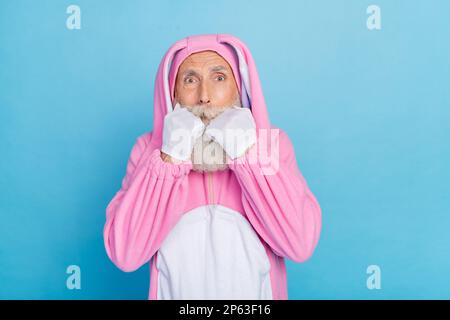 Foto di impressionato spaventato pensionato ragazzo vestito coniglietto kigurumi mordente dita isolato di colore blu sfondo Foto Stock