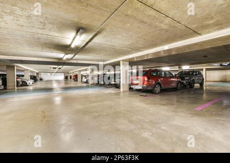 un parcheggio sotterraneo con auto parcheggiate nei garage e persone che camminano attraverso lo spazio per prendere le loro corse Foto Stock