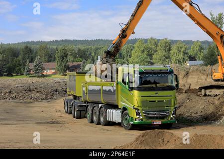 L'escavatore cingolato carica il terreno sul rimorchio a cassetta per camion Volvo FH16 verde in un giorno d'estate. Spazio di copia rimasto. Salo, Finlandia. Agosto 27, 2022. Foto Stock