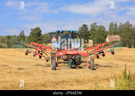 Contadino che lavora sul campo con il trattore e il doppio rastrello rotante Kverneland Taarup, rastrellando paglia secca in un giorno di tarda estate. Salo, Finlandia. Agosto 27, 2022. Foto Stock