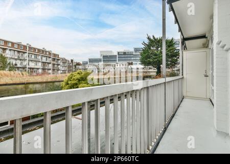 un balcone con alcuni edifici sullo sfondo e un fiume che lo attraversa, visto dalla finestra di un appartamento Foto Stock