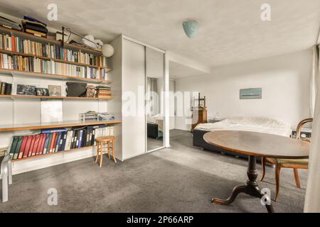 Amsterdam, Paesi Bassi - 10 aprile 2021: Un soggiorno con libri sugli scaffali e un tavolo rotondo davanti alla libreria pieno di libri Foto Stock