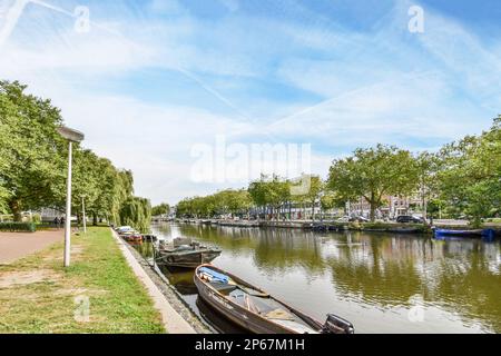 alcune barche attraccano sul lato di un fiume con alberi sullo sfondo e persone che camminano lungo il bordo dell'acqua Foto Stock
