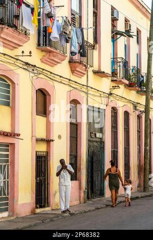 Uomo luci sigaro in strada tipica, colorato lavaggio drappeggiato su balconi, Old Havana, Cuba, Indie occidentali, Caraibi, America Centrale Foto Stock