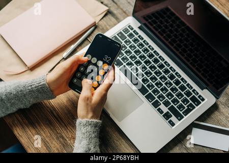 Donna irriconoscibile lavora utilizzando la calcolatrice e il computer portatile sul posto di lavoro. Foto Stock