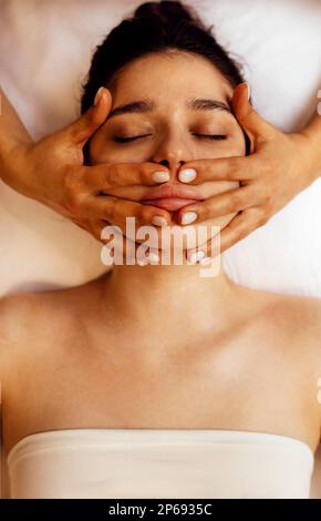 Primo piano ritratto di una giovane bella donna che ottiene il massaggio facciale. La bruna femmina gode di questa procedura. Trattamento spa. Te stesso e la cura della pelle c Foto Stock