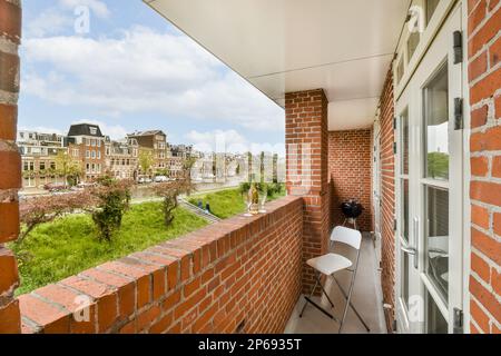 un balcone con pareti in mattoni rossi e finiture bianche intorno alle finestre, che si affaccia su una strada urbana in lontananza Foto Stock