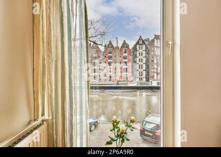 una vista dalla finestra di una stanza con un fiore in esso e gli edifici sull'altro lato del fiume Foto Stock