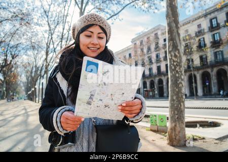 Una giovane ragazza turistica asiatica che cerca indicazioni stradali in una mappa cartacea visitando una città europea in un fine settimana. Vista frontale di una donna che guarda una posizione su una guida in un viaggio di vacanza. Concetto di viaggio. Foto di alta qualità Foto Stock