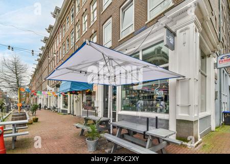 un'area esterna con tavoli e ombrelloni sul marciapiede di fronte ad un edificio in mattoni dipinto di bianco Foto Stock
