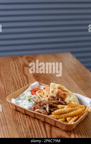 Souvlaki greco servito con patatine fritte e yogurt bianco nel ristorante fast food. Cibo tradizionale di strada dalla Grecia servito su piastra di carta riciclabile Foto Stock