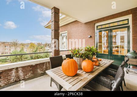 due zucche sedute su un tavolo di legno davanti ad un muro di mattoni con porte verdi e finestre dietro di loro Foto Stock