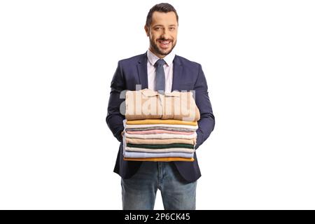 Giovane uomo che tiene un mucchio di vestiti piegati e sorridente alla macchina fotografica isolata su uno sfondo bianco Foto Stock