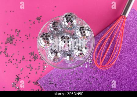 Festa rave, biglietto di auguri concetto. Frusta da cucina rosa con palline da discoteca lucenti e decorative in piccole stelle d'argento su sfondo magenta. Vista dall'alto, disposizione piatta. Foto Stock