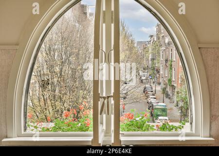 Amsterdam, Paesi Bassi - 10 aprile 2021: Vista dall'esterno da una finestra con fiori sulle davanzali e gli alberi nella zona arrotondata Foto Stock