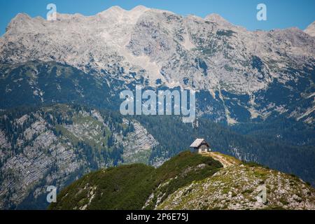 Una casa bianca è arroccata sulla cima del Parco Nazionale del Triglav montagna che si affaccia su un lussureggiante, campo verde sotto Foto Stock