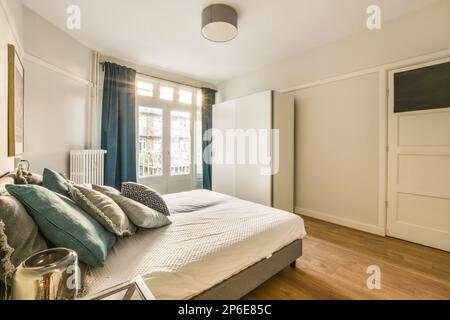 una camera da letto con pavimento in legno e drappeggi blu appesi alla parete dietro e' un letto che ha due cuscini Foto Stock