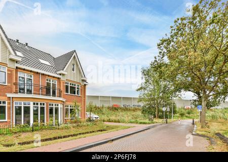 una strada con case sullo sfondo e alberi su entrambi i lati, lungo una strada lastricata vuota in mattoni che conduce ad un parcheggio Foto Stock