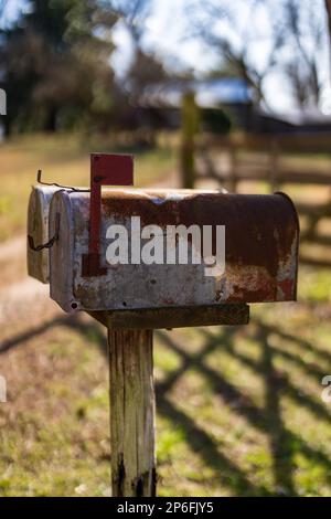 Una cassetta postale in metallo antico montata su un palo di legno, caratterizzata da un tradizionale top rosso con una finitura afflitta Foto Stock