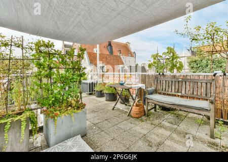 un patio esterno con piante e pentole a terra, sotto una tenda bianca sopra una panca di legno Foto Stock