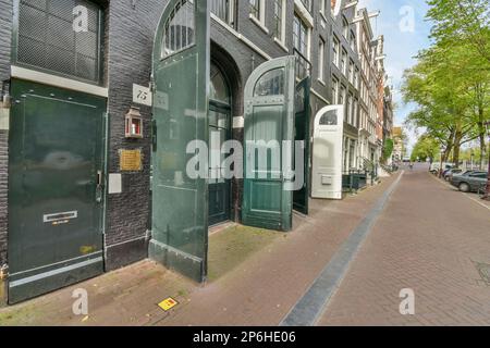 Amsterdam, Paesi Bassi - 10 aprile, 2021: Una strada in città con edifici su entrambi i lati e una porta aperta che conduce ad un parcheggio per le automobili Foto Stock