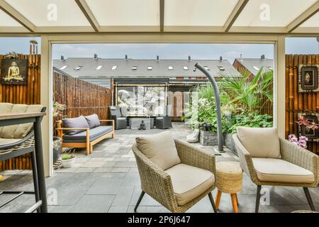 un'area soggiorno all'aperto con sedie, tavoli e una griglia nel cortile sul retro è visibile attraverso la porta di vetro Foto Stock