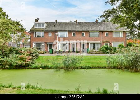 Amsterdam, Paesi Bassi - 10 aprile, 2021: Una casa che si trova nel mezzo di un giardino con acqua e piante intorno ad esso, in una giornata di sole Foto Stock