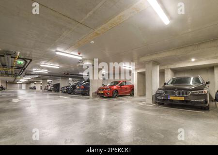 un parcheggio sotterraneo con auto parcheggiate nello spazio e persone che camminano sul marciapiede per prendere le chiavi dell'auto Foto Stock