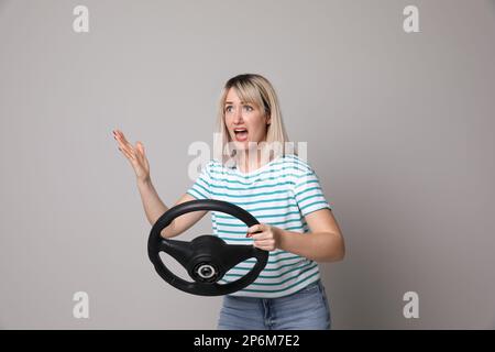 Donna emozionale con volante su sfondo grigio Foto Stock