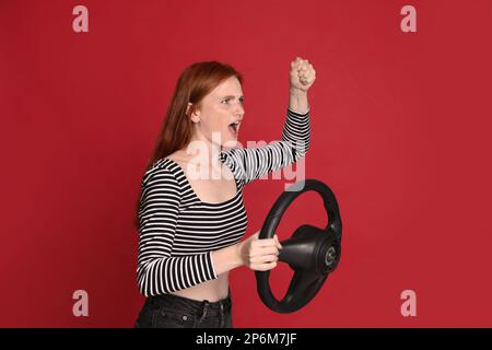 Giovane donna emozionale con volante su sfondo rosso Foto Stock