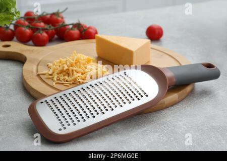 Tavola di legno con grattugia e formaggio su tavola grigia Foto Stock