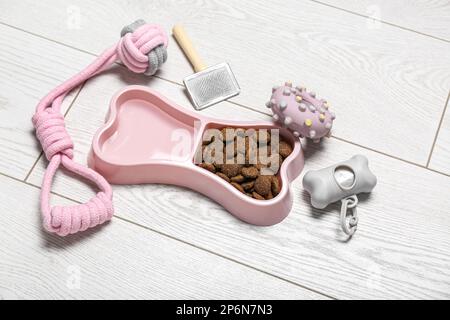 Set di accessori per la cura degli animali domestici e ciotola di pappe secche su sfondo di legno chiaro Foto Stock