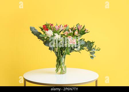 Vaso con bellissimi fiori di alstroemeria su tavolo vicino al muro giallo Foto Stock