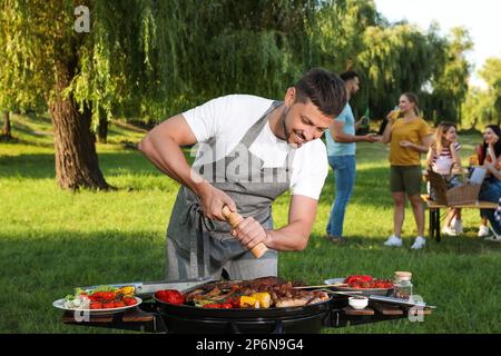 Uomo che cucina carne e verdure sul barbecue grill nel parco Foto Stock