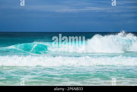 Vista dall'angolo basso delle onde tropicali turchesi dell'oceano che si infrangono e si infrangono vicino alla riva con cieli tempestosi in lontananza Foto Stock