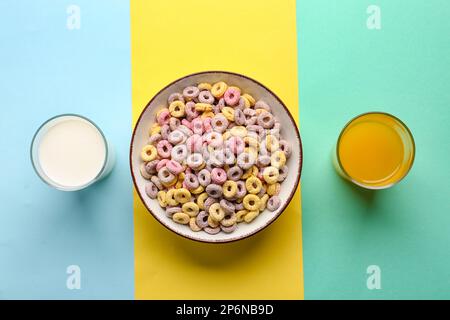 Ciotola con anelli di cereali, bicchieri di latte e succo su sfondo colorato Foto Stock