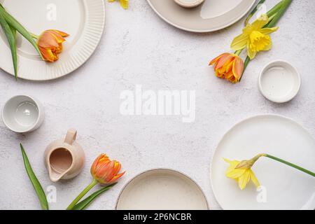 Cornice fatta di piatti puliti e bellissimi fiori su sfondo bianco grunge Foto Stock