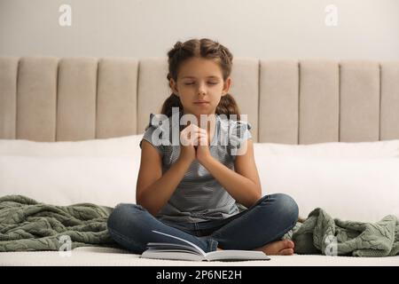 Ragazza carina che prega sopra la Bibbia in camera da letto Foto Stock