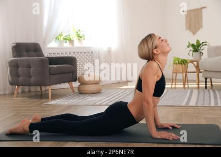 Bella donna che pratica yoga in stanza luminosa a casa Foto Stock