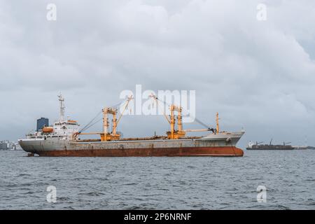 Una nave da carico nei mari sereni, il suo esterno usurato che mostra segni di erosione del mare, in quanto trasporta forniture vitali al vivace porto cittadino. Onde crash a Foto Stock