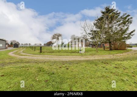 un campo erboso con case in lontananza e alberi sull'altro lato della strada, come visto da terra Foto Stock