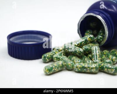 capsule con pillole verdi, gialle e bianche contenenti integratori vitaminici e nutrienti sparsi da una bottiglia blu isolata su sfondo bianco Foto Stock