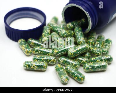 capsule con pillole verdi, gialle e bianche contenenti integratori vitaminici e nutrienti sparsi da una bottiglia blu isolata su sfondo bianco Foto Stock