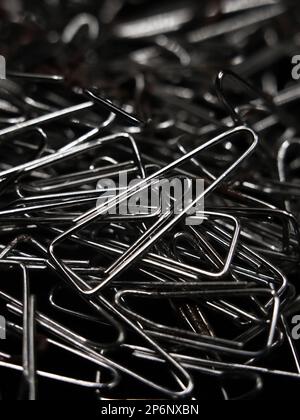 primo piano macro shot di una grande pila di clip di carta argento lucido a forma triangolare utilizzati per scopi aziendali o educativi sparsi in modo casuale intorno Foto Stock