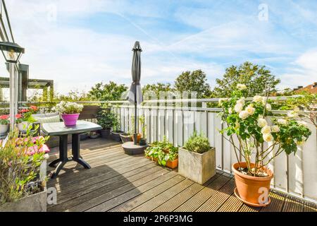 Amsterdam, Paesi Bassi - 10 aprile 2021: Un balcone con fiori in vaso sul tavolo e un ombrello nel cielo è blu, bianco e rosa Foto Stock
