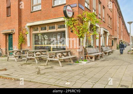 Amsterdam, Paesi Bassi - 10 aprile, 2021: Un edificio in mattoni con panchine e tavoli sul marciapiede di fronte, c'è una persona che cammina Foto Stock