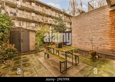 un'area esterna con tavoli e panchine al centro del cortile, accanto ad un edificio recintato Foto Stock